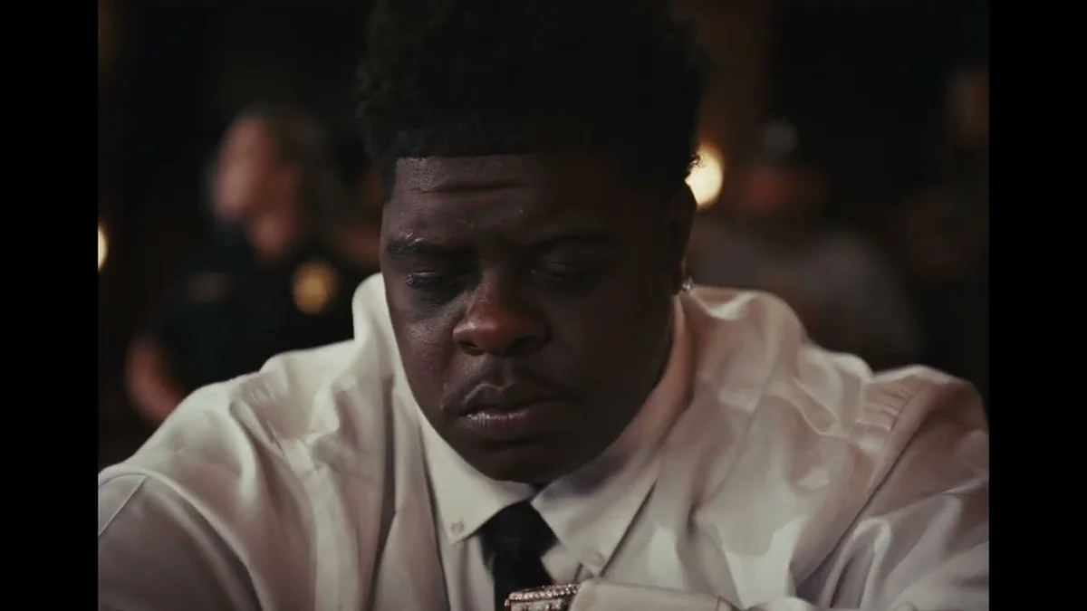 BigXthaPlug with head bowed in a shirt and tie in a dim room in the BURN music video